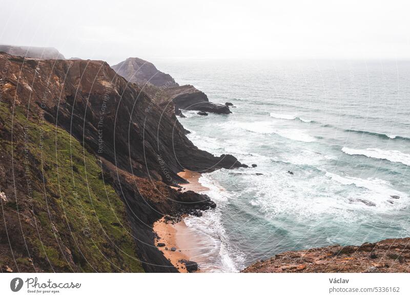 High limestone cliffs sinking into the Atlantic Ocean in the Algarve region, southwestern Portugal. Rainy weather. Wandering along the Fisherman Trail splash