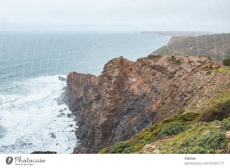 Adventurous man standing on the edge of a cliff enjoys the view of the Atlantic coast in the Odemira region of southwestern Portugal. Wandering the Rota Vicentina