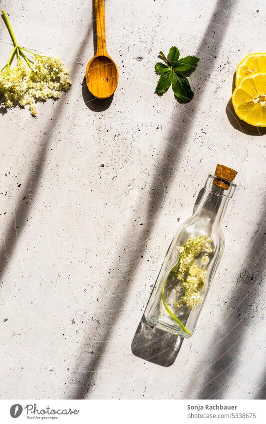 Ingredients for homemade elderflower syrup on a gray rustic table. Light and shadow. Top view. Elderflower Lemon Syrup Self-made Glassbottle Wooden spoon