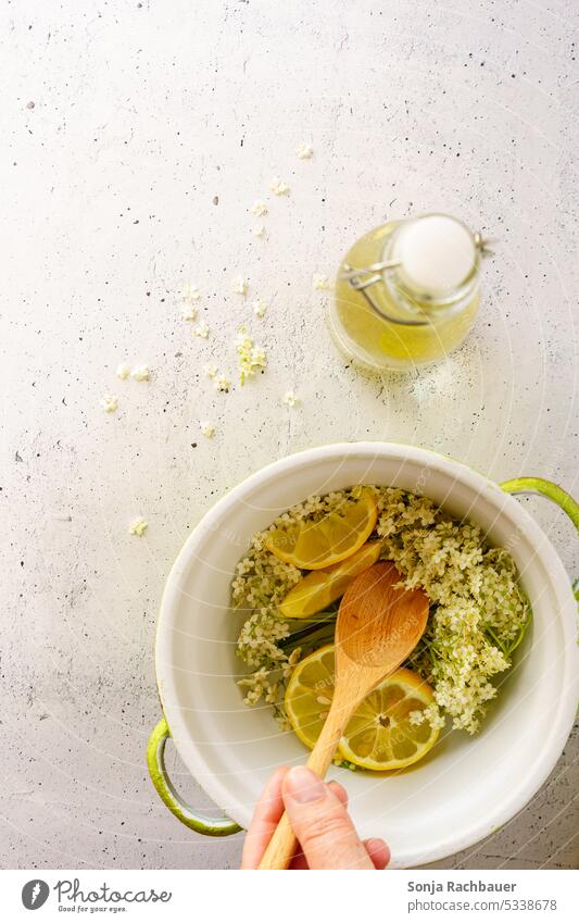 Fresh elderflowers and lemons in a saucepan. Top view. Elderflower Lemon Syrup Self-made Summer Beverage Yellow Wooden spoon Hand Stir Healthy Food Refreshment