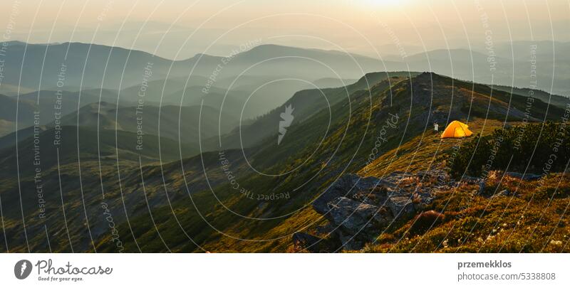 People spending summer vacation in mountains, standing by tent looking at sunrise over valley. Active couple hiking in mountains. Foggy mountain landscape view at sunrise