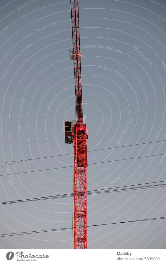 Red construction crane behind overhead wires at Deutschherrn Bridge in front of blue sky in the evening sun at Hafenpark and Hafenparkquartier at Hanauer Landstraße in the east end of Frankfurt am Main in Hesse, Germany