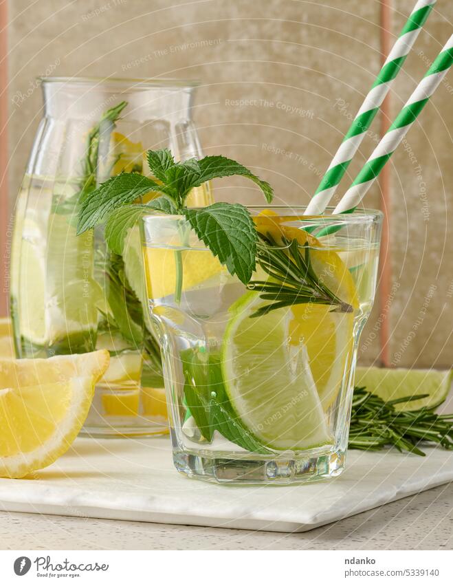 Lemonade in a transparent glass with lemon, lime, rosemary sprigs and mint leaves on a white background lemonade drink cocktail refreshment fruit ice green