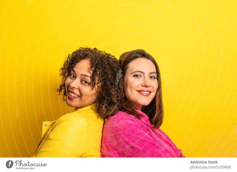 Cheerful multiethnic friends looking at camera against yellow background women girlfriend smile happy together cheerful friendship positive relationship bright