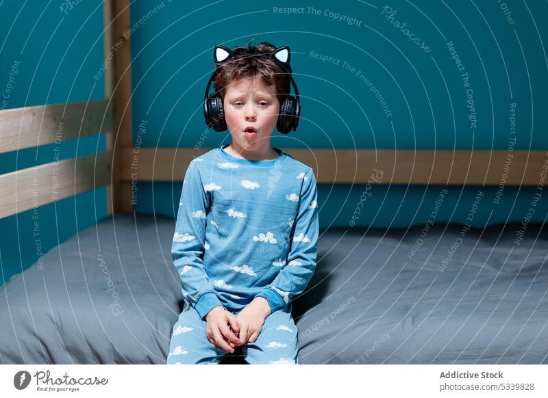 Cute child with headphones sitting on bed kid sing song music listen night wireless cute bedroom gadget childhood home device audio enjoy carefree melody