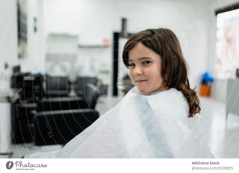 Happy child sitting in salon wearing cape girl smile kid fabric calm cute adorable relax preteen happy positive childhood cheerful daytime glad comfort wrap