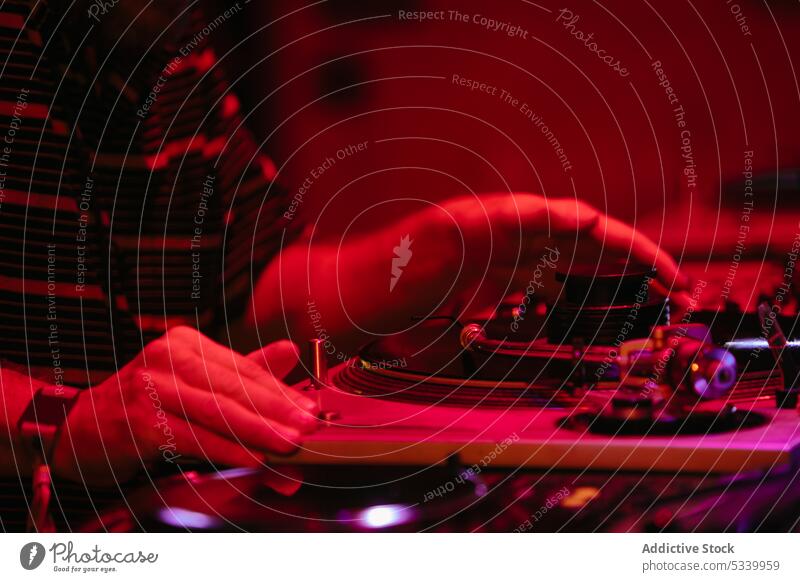 Crop DJ putting on record in red neon man dj party music console night mix equipment entertain play audio professional turntable using perform event panel male