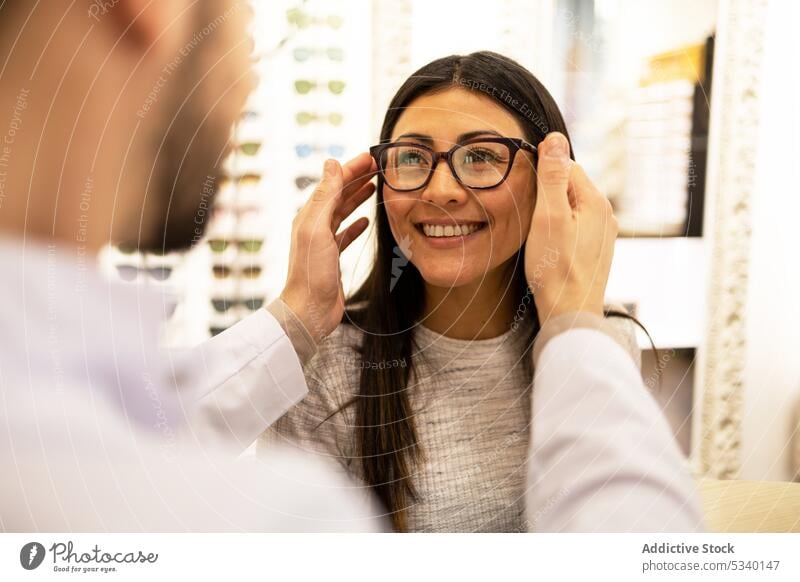 Happy woman trying on different eyeglass frames in store optician assist eyeglasses buy choose customer eyewear smile shop cheerful try on choice uniform