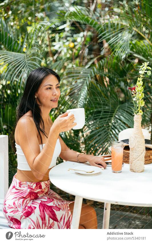 Cheerful woman drinking coffee in outdoor cafe summer resort enjoy happy tropical smile positive coffee break tulum mexico mexican asian young female cheerful