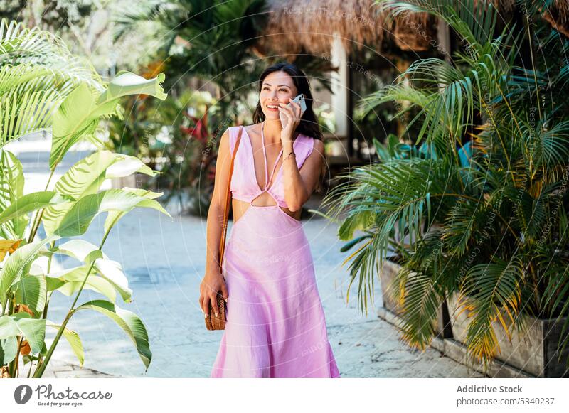 Happy woman talking on smartphone on street with palms garden smile tropical summer speak happy phone call female mexican mexico japanese asian tulum