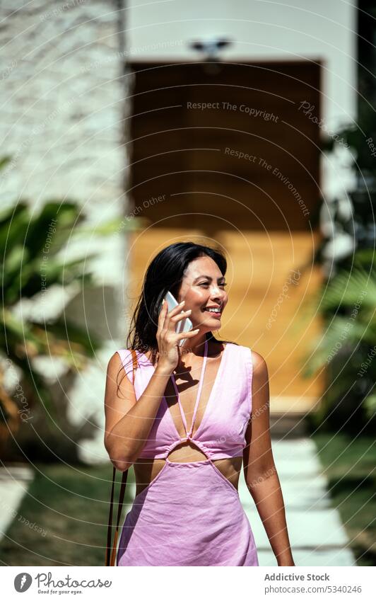 Cheerful woman speaking on smartphone during walk garden smile talk palm tropical summer happy phone call female mexican mexico japanese asian tulum young