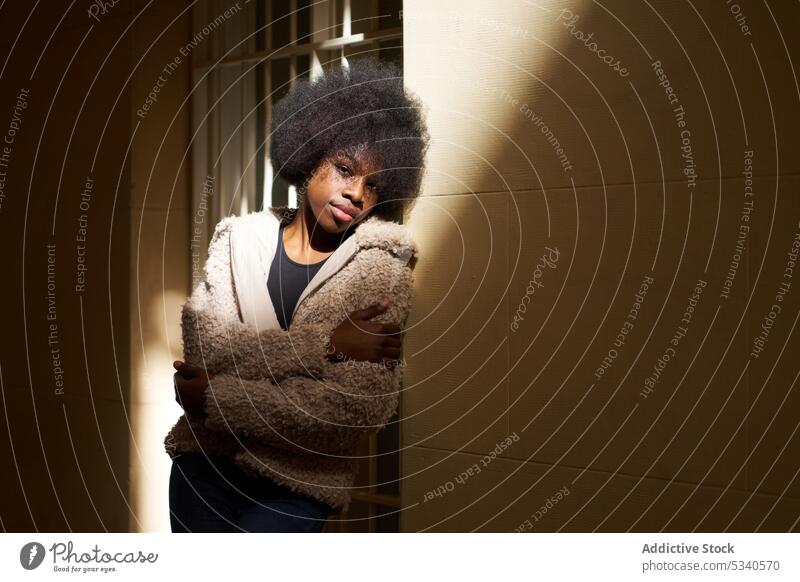 Dreamy teenager in Afro hairdo and cozy casual clothes standing with crossed arms and closed eyes dreamy shadow mindfulness ponder contemplate arms crossed