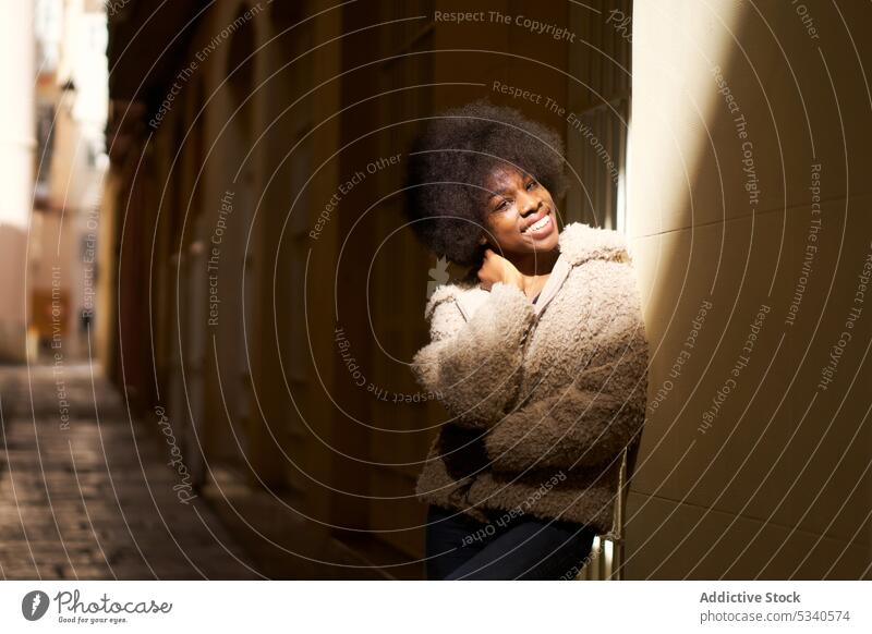 Dreamy teenager in Afro hairdo and cozy casual clothes standing with crossed arms dreamy shadow mindfulness cheerful ponder contemplate arms crossed smile