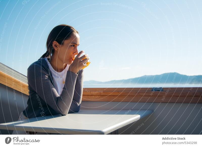 Thoughtful woman drinking fresh orange juice on balcony pensive calm rest relax admire terrace female beverage casual thoughtful enjoy young picturesque