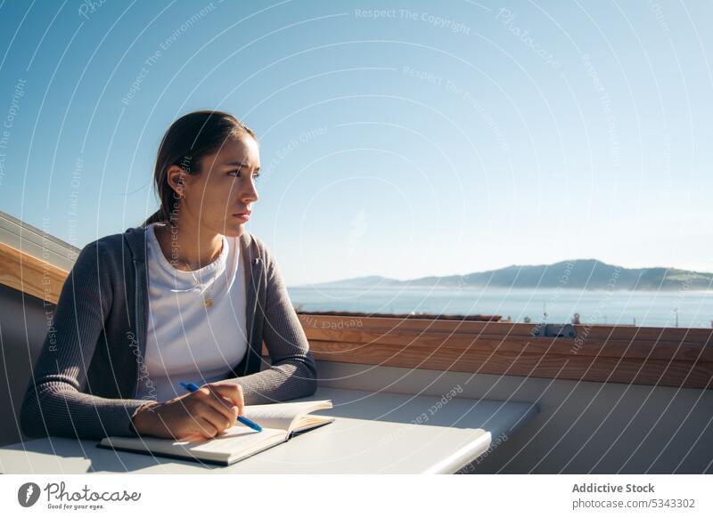 Dreamy woman taking notes in notebook on balcony take note notepad write student think terrace study thoughtful female young pensive concentrate freelance plan