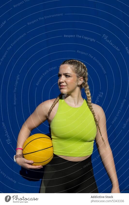 Sportswoman standing with basketball on blue wall sportswoman break confident athlete training relax wellness workout female player sportswear young active