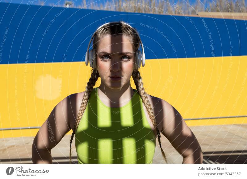 Young woman listening to music in headphones portrait braid confident shadow color wall calm young female bright vivid emotionless style colorful yellow trendy