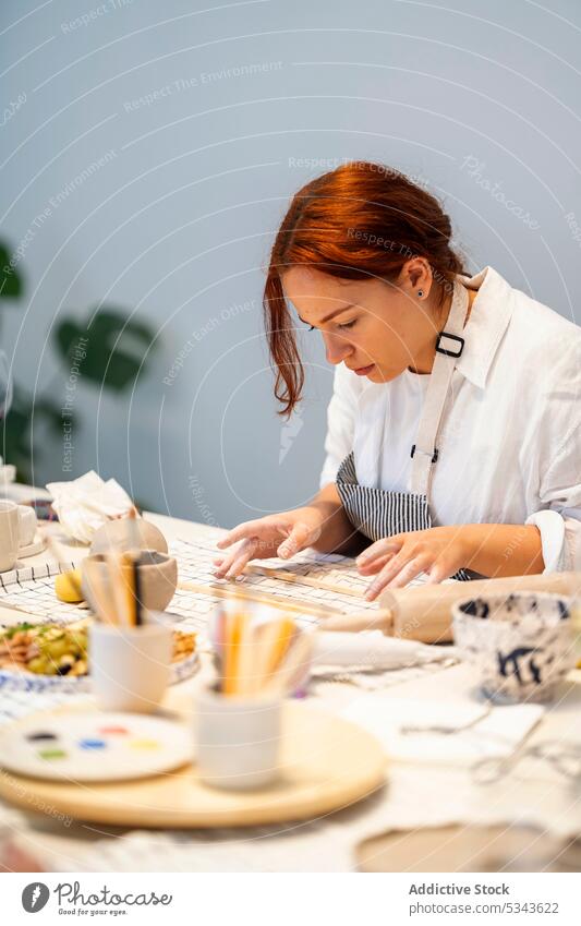 Focused woman rolling clay during work process create pottery artisan craft handmade clayware craftswoman workshop female skill young hobby handicraft crockery