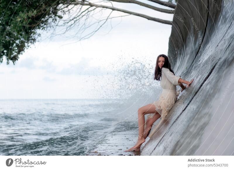 Carefree woman on stone fence near sea rest summer vacation relax lean tourist barefoot ocean female eyes closed coast water calm young holiday resort travel