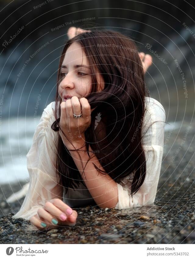 Dreamy woman lying on seashore and looking away dreamy nature charming rest thoughtful calm relax lean on hand brunette stone female coast summer pensive young