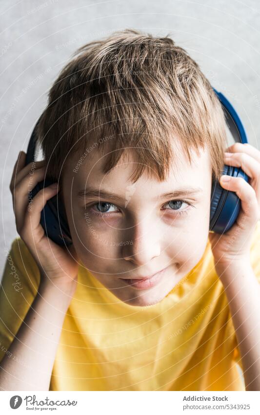 Front view of cute kid looking at camera while listening to music beautiful boy child ear eyes face headphones human over-ear person portrait t-shirt teenager