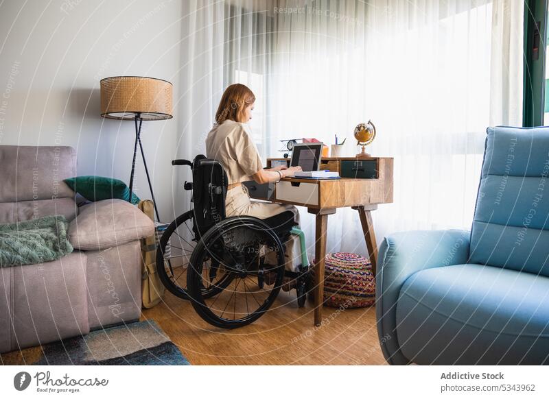 Young woman sitting on wheelchair while taking notes from laptop notebook take note write freelance sofa living room home using gadget at home planner work