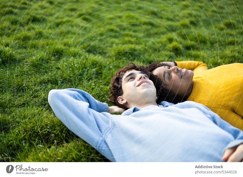 Happy diverse friends lying on grass in park man woman friendship smile hand behind back relax daylight daytime multiracial multiethnic nature lawn summer young