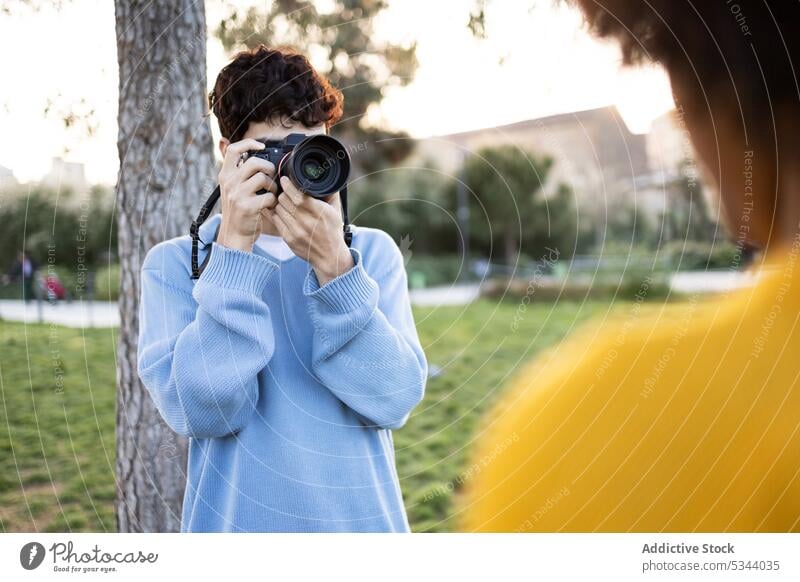 Young man shooting photos near tree on green grass take photo photo camera photographer park photography hobby professional capture daytime trunk summer nature