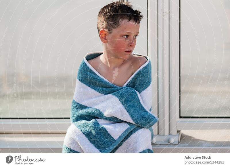 Cute boy in towel on poolside resort summer vacation holiday child fence kid tropical calm rest recreation sun weekend wrap wooden pensive summertime serious