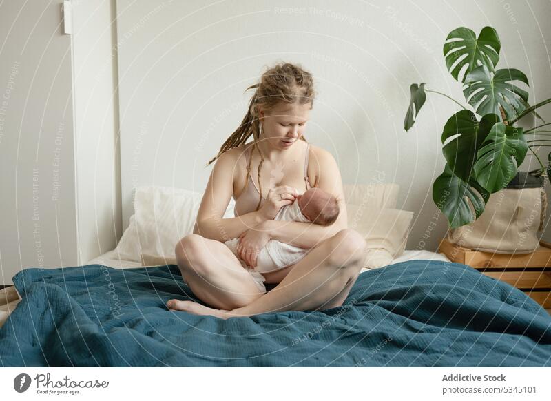 Woman breastfeeding infant sitting on bed woman mother baby newborn mom childcare cozy female comfort innocent motherhood together bedsheet lady legs crossed