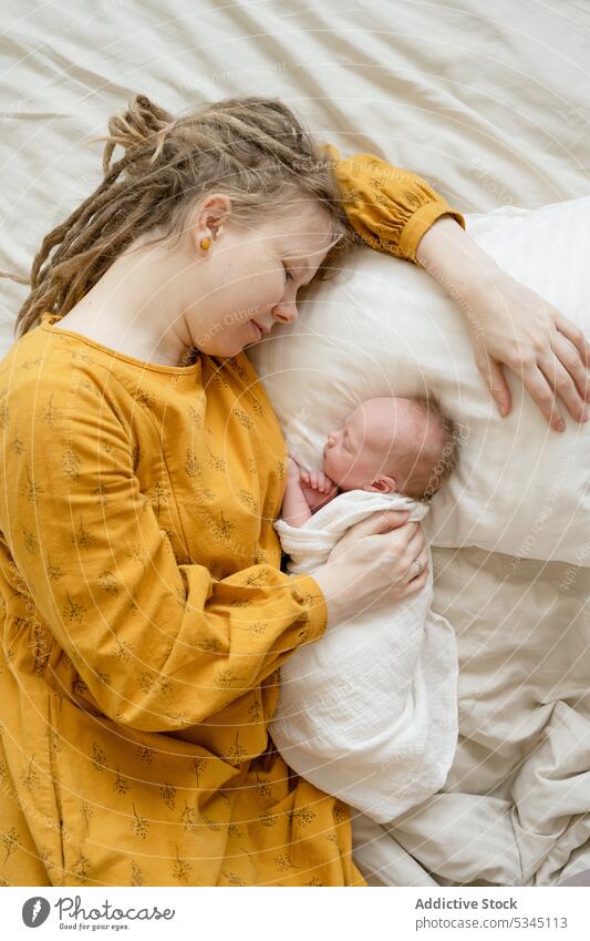 Woman lying on bed with baby woman mother sleep infant newborn mom comfort cozy hug female child innocent vulnerable peaceful asleep embrace bedsheet motherhood