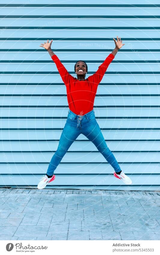 Excited woman jumping with raised arms model leap excited cheerful smile city street female black african american celebrate joy thrilled win success victory