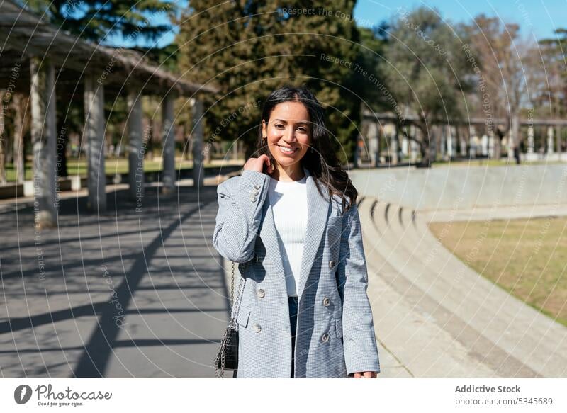 Smiling ethnic woman standing on walkway portrait smile glad positive content pathway pleasant delight summer young daytime tree female hispanic sunlight happy