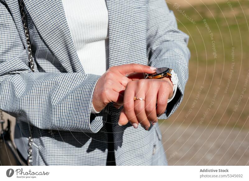 Unrecognizable woman touching wristwatch while standing in park time check punctual city walk checkered summer style nature female street jacket trendy late