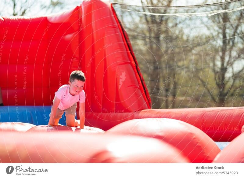 Smiling child on knees and playing in bouncy house kid smile summer colorful happy adorable delight inflatable boy cheerful bright tree joy positive daytime