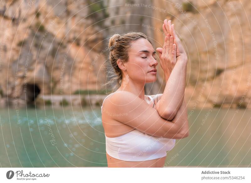 Fit woman practicing yoga on pier calm practice zen healthy asana harmony wellness meditate lake mountain Charco Azul pose female Spain Valencia eagle pose