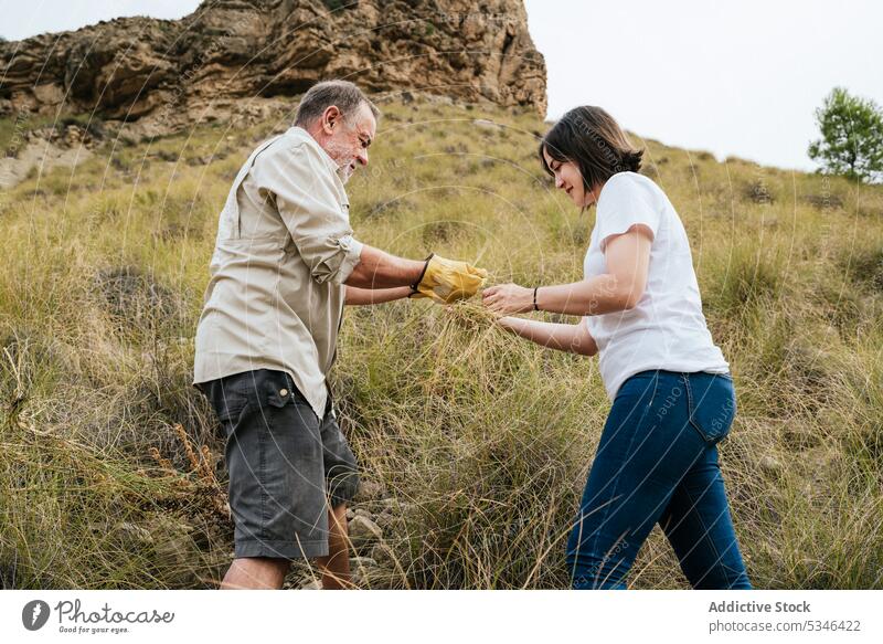 Happy farmers harvesting esparto grass at hillside man woman collect together highland slope daughter father smile family business agriculture young senior work