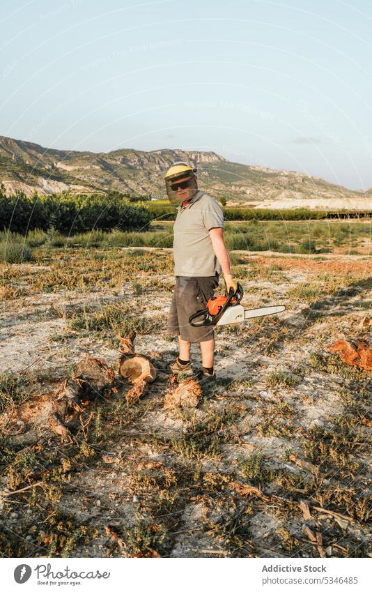 Farmer cutting firewood with chainsaw in countryside farmer field prepare man trunk male tree mountain nature highland rural equipment tool instrument modern