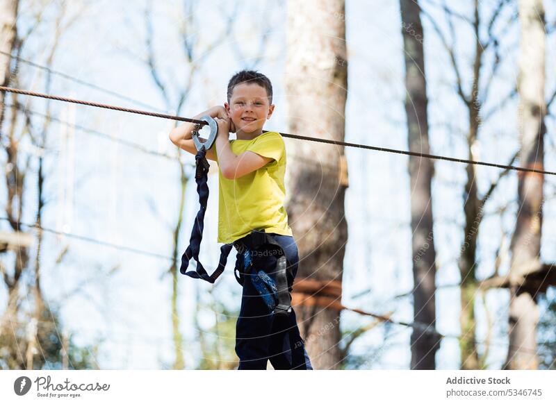 Cheerful boy standing on rope bridge in park child summer safety kid cheerful nature equipment weekend activity active childhood preteen entertain forest