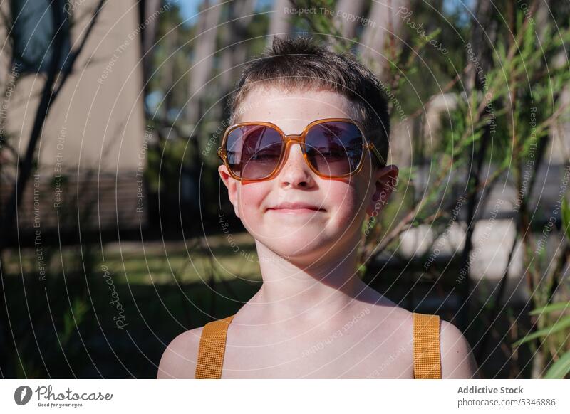 Stylish boy in sunglasses standing near plants nature summer vacation happy confident child garden eyewear eyes closed naked torso delight green calm young