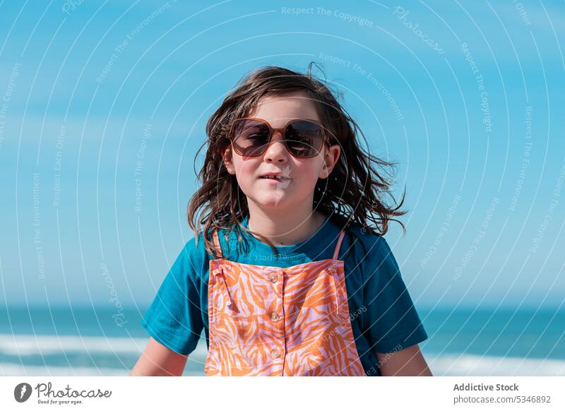 Stylish preeteen girl in sunglasses standing near sea seashore trendy style beach sunlight summer seaside dream coast blue sky preteen peaceful carefree serene