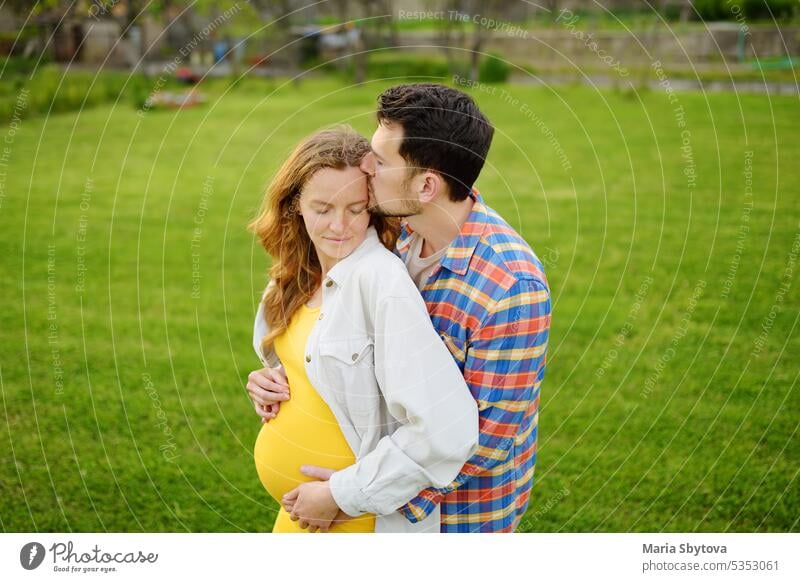 Young family is expecting a baby. Happy couple of parents-to-be walking together. Husband embracing wife gently and holding her belly enjoying. pregnant woman