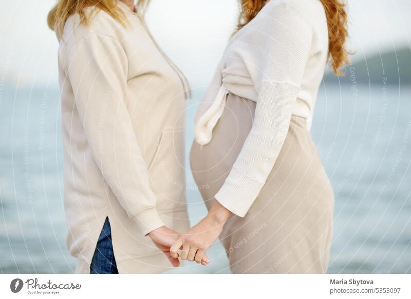 Senior mother and her adult beautiful pregnant daughter are walking together on the sea shore. A happy meeting of a mom and her grown child. senior people