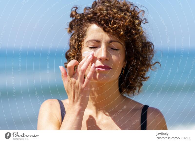 Sensual woman applying sunscreen on face beach sunblock summertime protect skin care sea vacation sensual female young curly hair bikini cream seashore sunbath