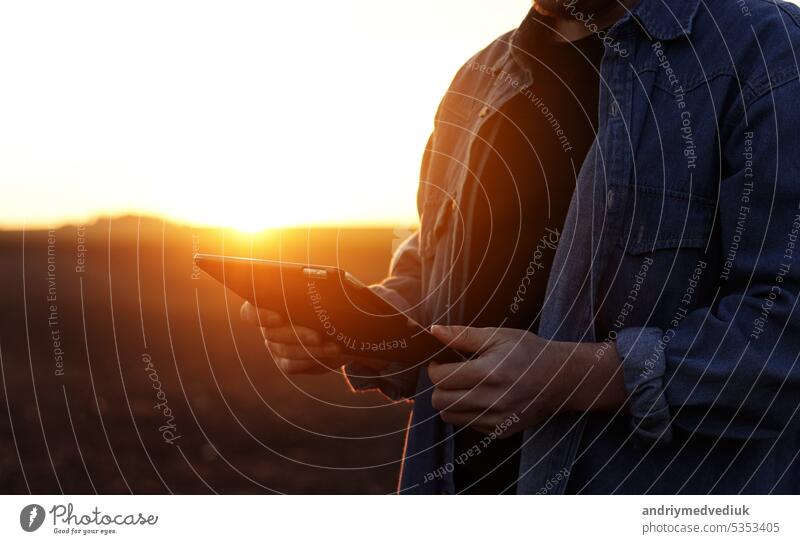 Cropped shot of male farmer's hands use digital tablet on plowed field for control of soil quality, land readiness for sowing crops and planting vegetables. Smart farming technology and agriculture