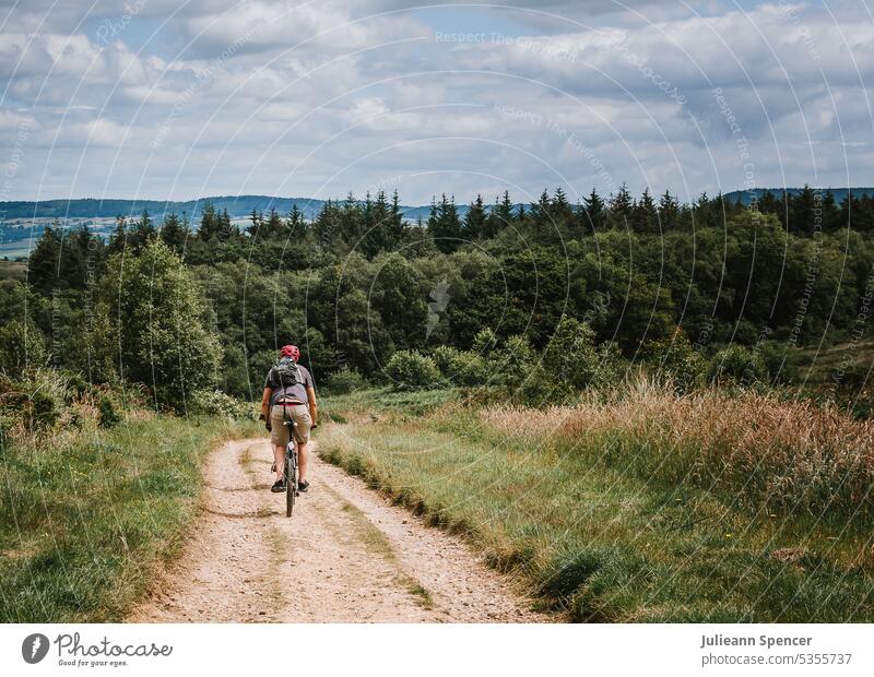 Man bike riding towards forest down dirt track bike rider man riding bike short backpack biking biking on dirt bikes bike lane trees wood bicycle cyclist