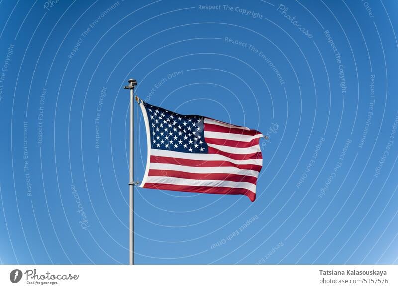 The flag of the United States of America flutters in the wind against a clear blue sky. Waving USA flag american flag usa flag pole 911 remembrance