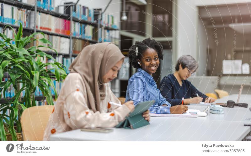 Multiethnic group of students sitting in a library and studying together real people teenager campus positive exam knowledge confident academic adult lifestyle