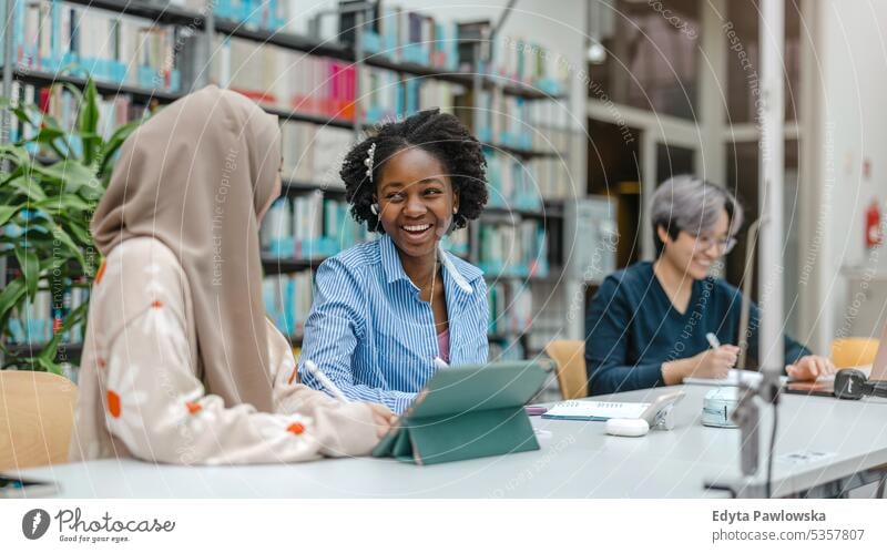 Multiethnic group of students sitting in a library and studying together real people teenager campus positive exam knowledge confident academic adult lifestyle