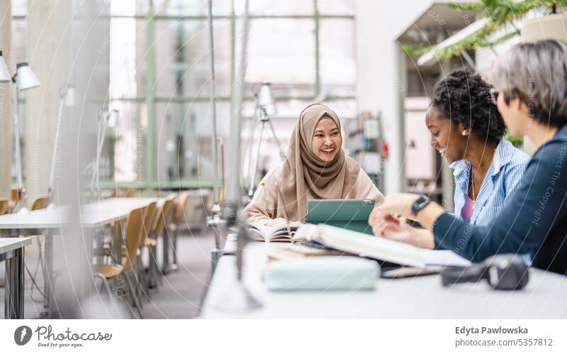 Multiethnic group of students sitting in a library and studying together real people teenager campus positive exam knowledge confident academic adult lifestyle